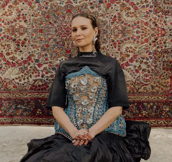 Il s'agit de Nawel Ben Kraïem. Elle a les cheveux longs et porte un corsets ornés de perles et de sphères argentés. Elle a aussi beaucoup de bijoux aux oreilles.