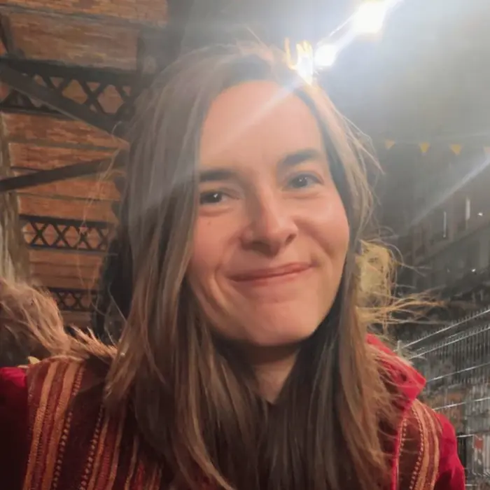 Sur cette image apparaît Yulia Arsen. Elle a les cheveux longs, lisses et  châtains et porte une veste rouge à rayures oranges. Elle arbore un sourire.