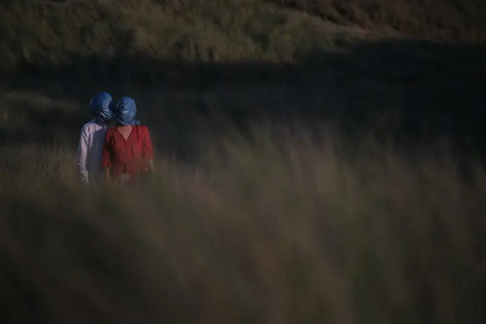 Sur ces images on voit un couple attaché par la tété avec du plastique. Ils sont au milieu de l'herbe, sur une falaise.