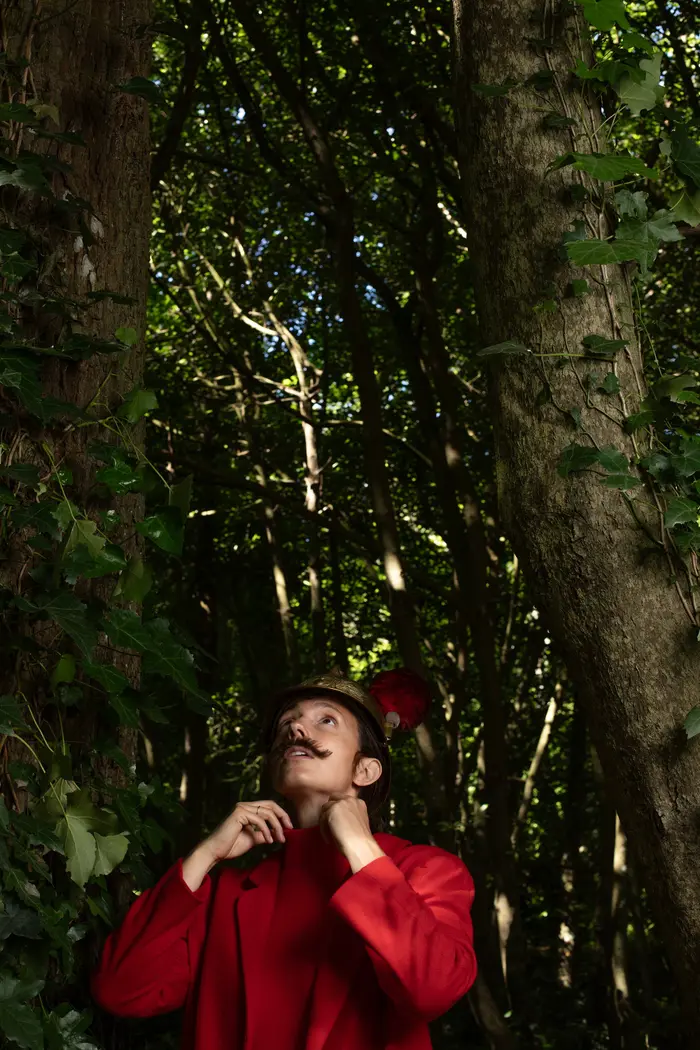 Sur cette image il y a une personne regardant le ciel , elle est habillée en rouge avec un ancien casque de sapeur pompier 