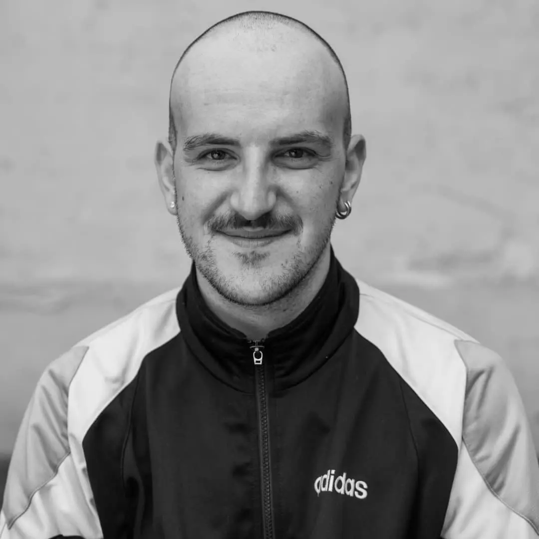 C'est une photo de portrait de Thibaut Galis en noir et blanc. Il est chauve, il porte une veste sportswear et arbore un joli sourire.