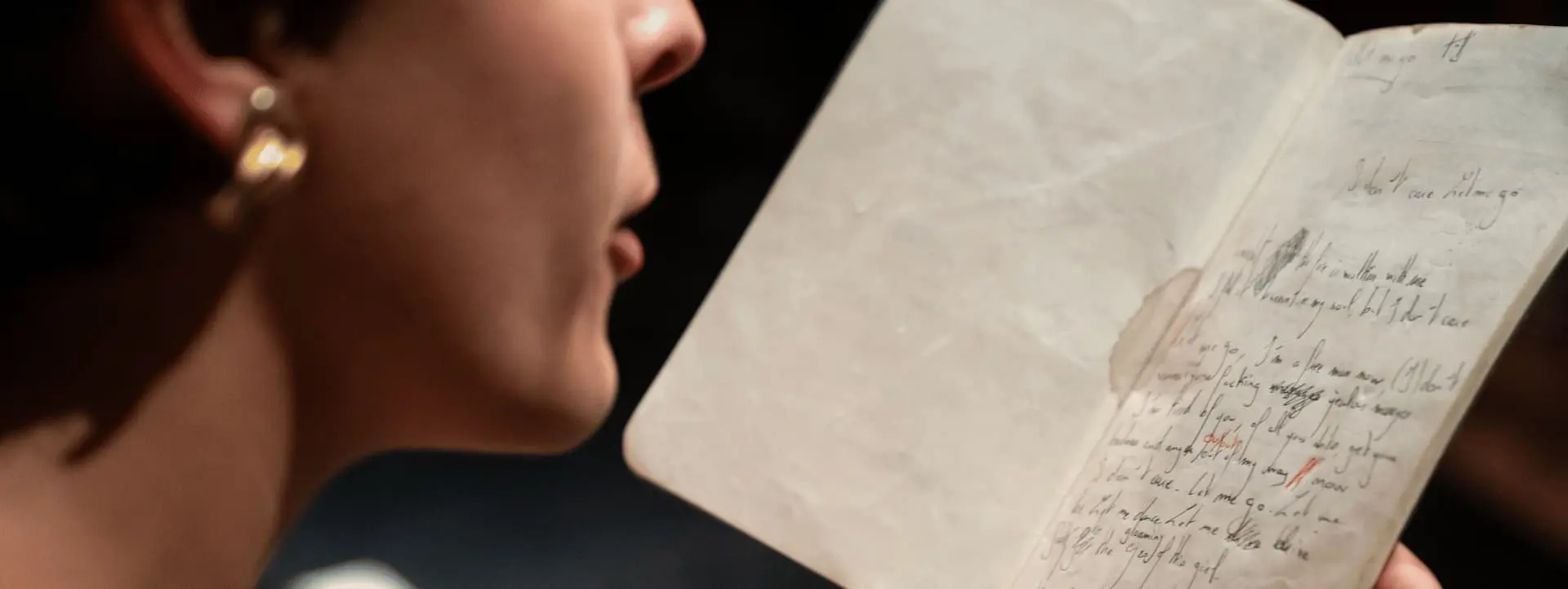 Une personne est en train de lire un carnet sur lequel il y a des écritures. On ne voit que le bas de son visage, et ses mains qui tiennent le carnet.