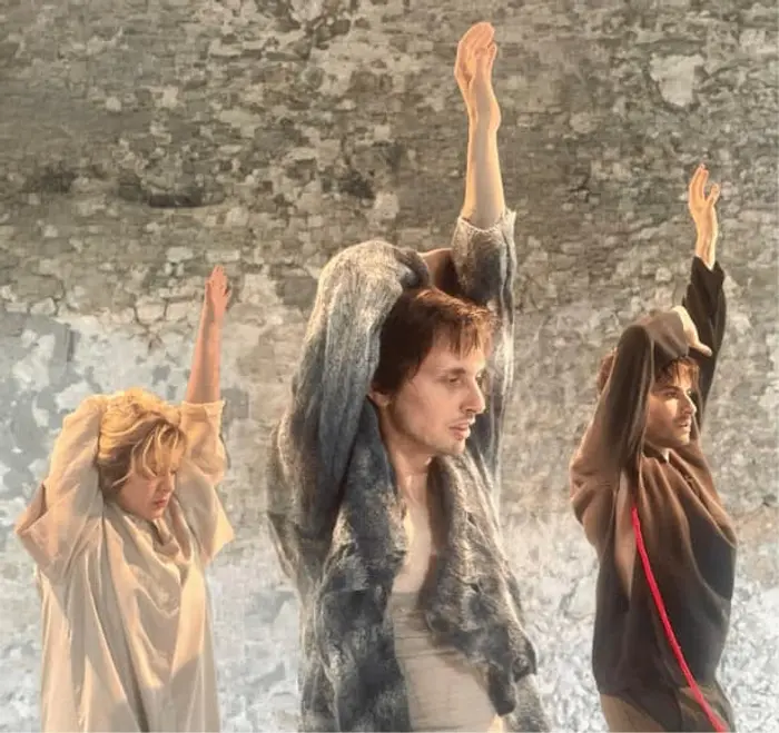 2 danseurs et 1 danseuse tendent le bras gauche vers le ciel. Ils sont tous tournés vers la droite, on les voit de 3/4. Leur autre bras passe par dessus la tête pour venir poser sa main sur le coude du bras gauche levé.