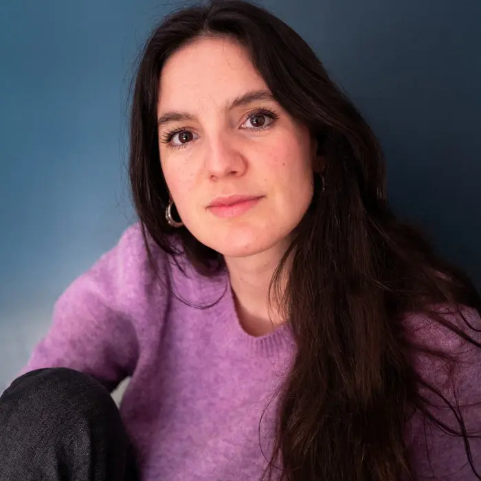 Sur cette image on voit Asja Nadjar. Elle a les cheveux longs bruns et porte un pull violet.