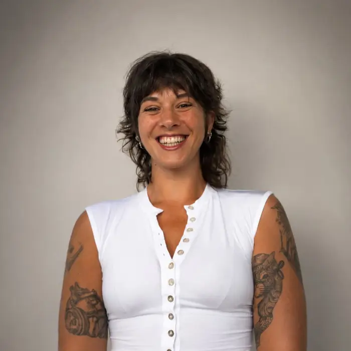Dafne est au centre de l'image, elle porte un débardeur blanc. Elle a les cheveux mi-longs et arbore un grand sourire.