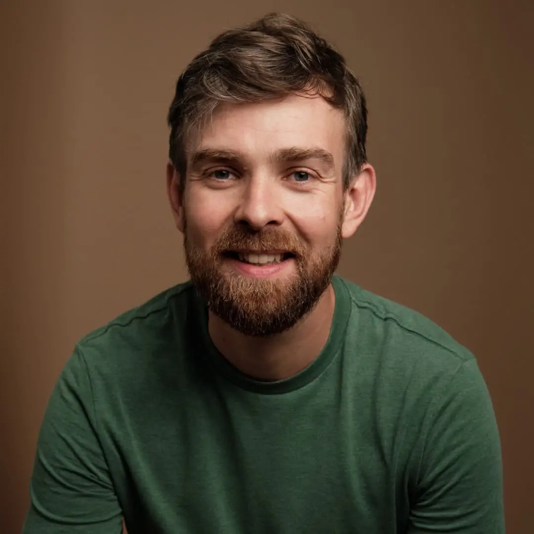 Sur cette image on voit Sylvain Gaudu, devant un mur marron. Il est vêtu d'un tee-shirt vert et arbore un sourire.