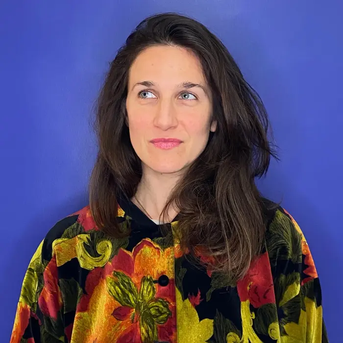 Sur cette image on voit Margaux Amoros. Elle a les cheveux bruns, porte une veste à fleurs et arbore un sourire.