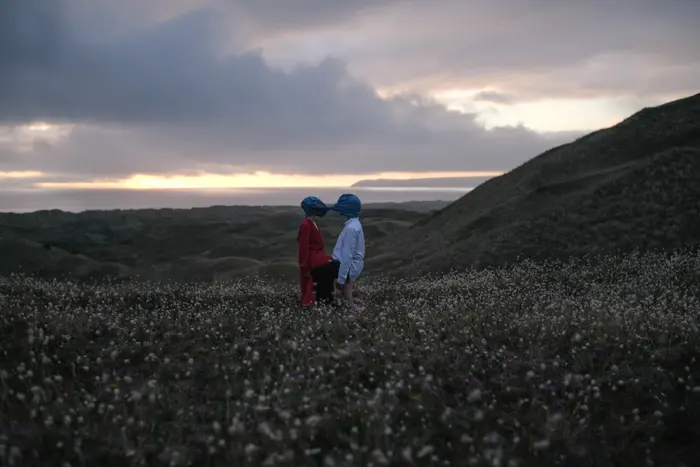 Sur ces images on voit un couple attaché par la tété avec du plastique. Ils sont au milieu de l'herbe, sur une falaise.