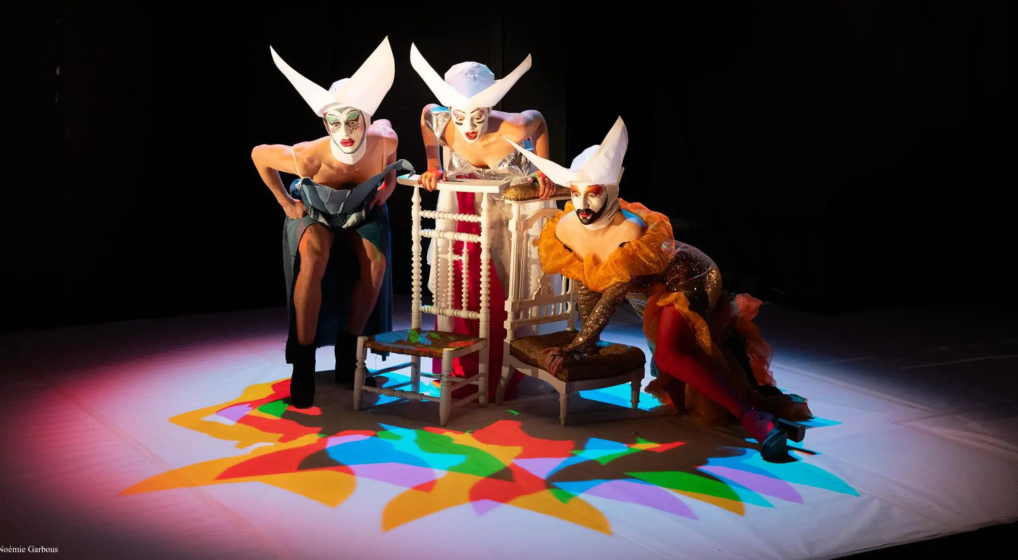 Il y a trois personnes  et prennent des poses très expressives.Les lumières projettent des couleurs au sol