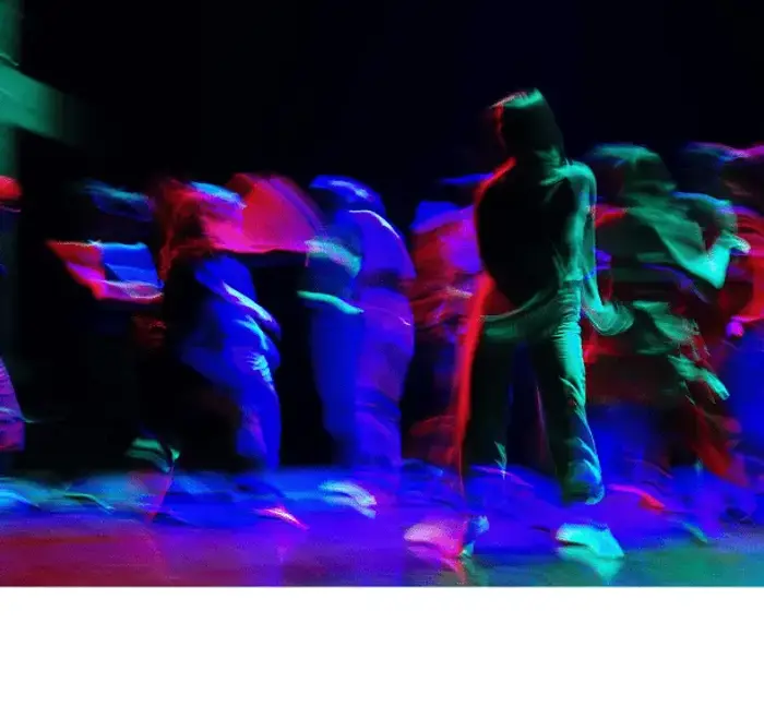 Des personnes dansent sur le plateau. Elles sont de toutes les couleurs car il y a beaucoup de projecteurs. Toutes les silhouettes sont floues. C'est comme si l'appareil photo avait pris au ralenti les mouvements de danse.