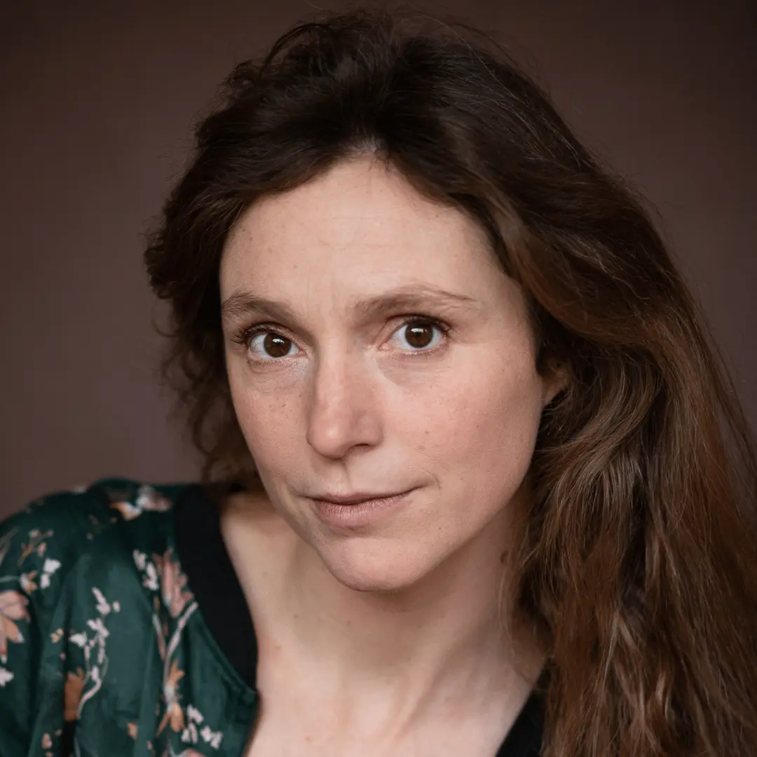 Sur cette photo apparaît le visage de Camille Demoures. Elle a les cheveux longs et châtain et porte une veste à fleurs. 