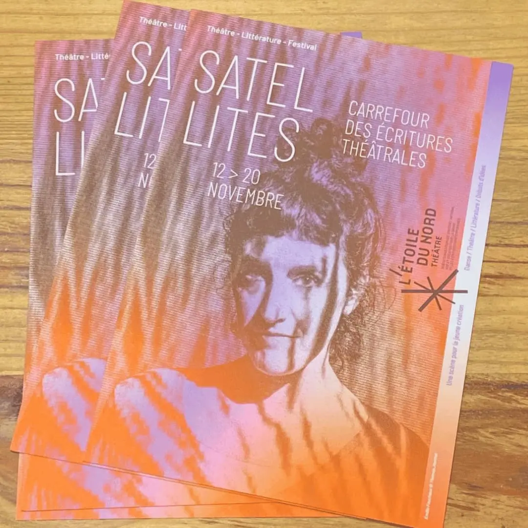 C'est une photo d'une pile de flyers Satellites. On y voit le portrait d'Emilie Faucheux qui regarde son auditoire de face. Elle a un chignon et porte un tee-shirt manche longue dont on ne voit que le col rond. Le flyer est aux couleurs de saison c'est à dire qu'il y a un dégradé du orange vers le violet en contrastant avec les silhouettes en marron.