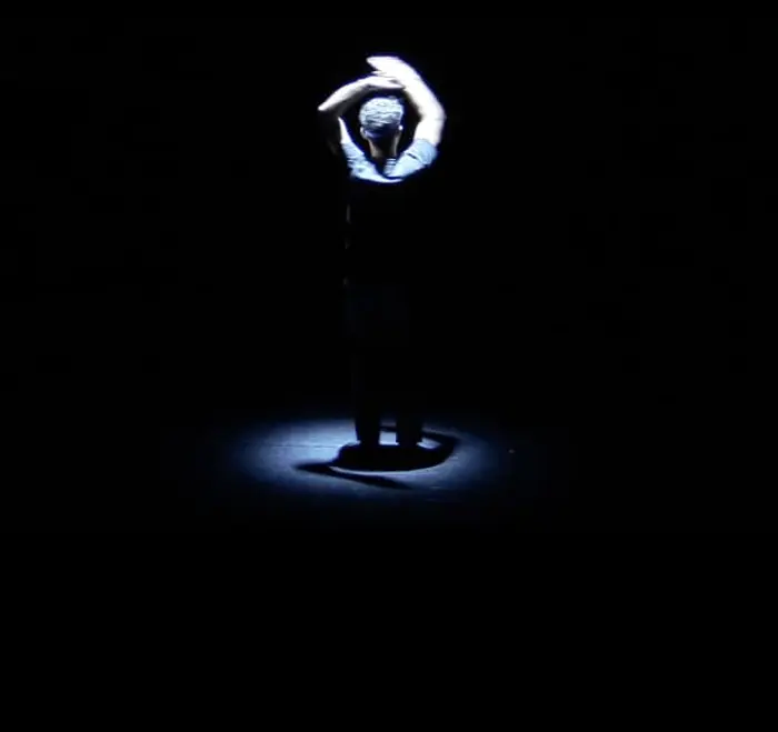 Un homme tourne et une lumière lui vient du dessus pour ne projeter que l'ombre de ses bras au sol.