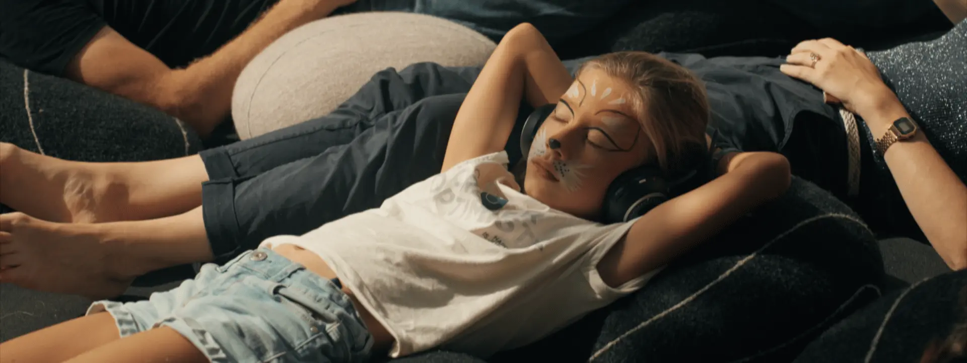Sur cette image on voit une petite fille couchée sur des coussins. Elle a les yeux fermés et a un casque sur les oreilles.